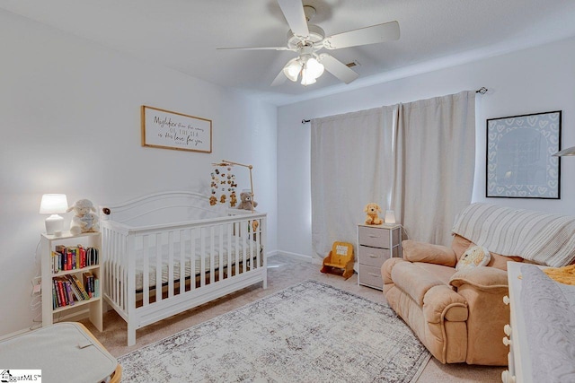 carpeted bedroom with a nursery area, ceiling fan, and baseboards