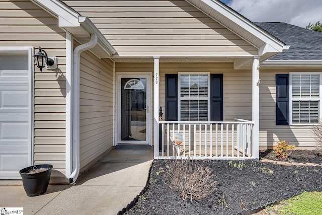 doorway to property featuring a garage, a shingled roof, and covered porch