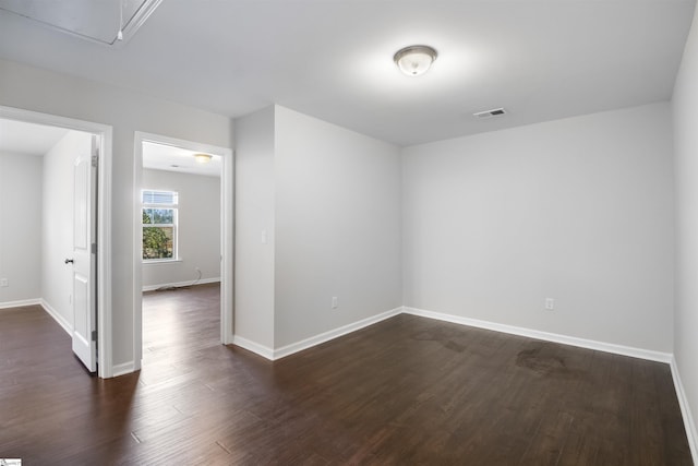 empty room with baseboards, attic access, visible vents, and dark wood-type flooring