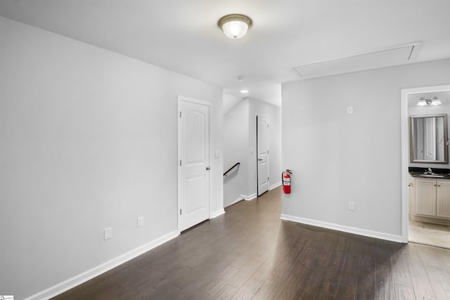 unfurnished room with attic access, baseboards, a sink, and wood finished floors