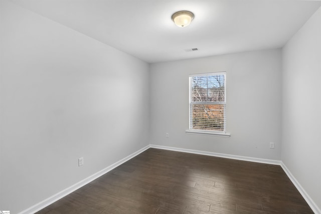 empty room featuring visible vents, dark wood finished floors, and baseboards