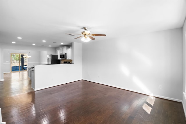 unfurnished living room with ceiling fan with notable chandelier, dark wood finished floors, visible vents, and baseboards