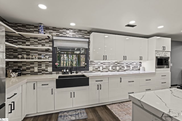 kitchen with wall oven, white cabinets, decorative backsplash, dark wood-style flooring, and a sink