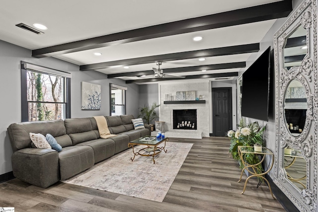 living room with visible vents, ceiling fan, wood finished floors, a fireplace, and beam ceiling