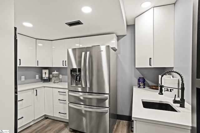 kitchen with stainless steel fridge, visible vents, wood finished floors, white cabinetry, and a sink