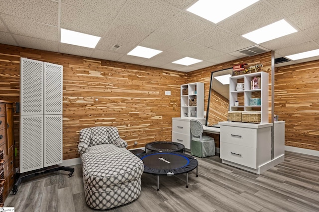 living area with wood walls, a drop ceiling, wood finished floors, and visible vents