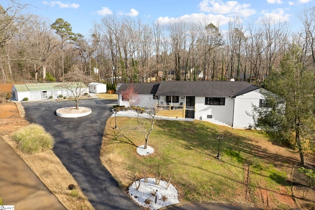 ranch-style home featuring driveway, a porch, a front lawn, and an outbuilding