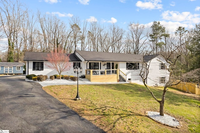 ranch-style home featuring aphalt driveway, a front yard, covered porch, and fence