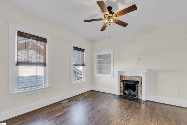 unfurnished living room featuring built in features, a stone fireplace, baseboards, and wood finished floors