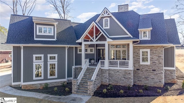 craftsman-style home featuring stone siding, a shingled roof, a chimney, and a porch