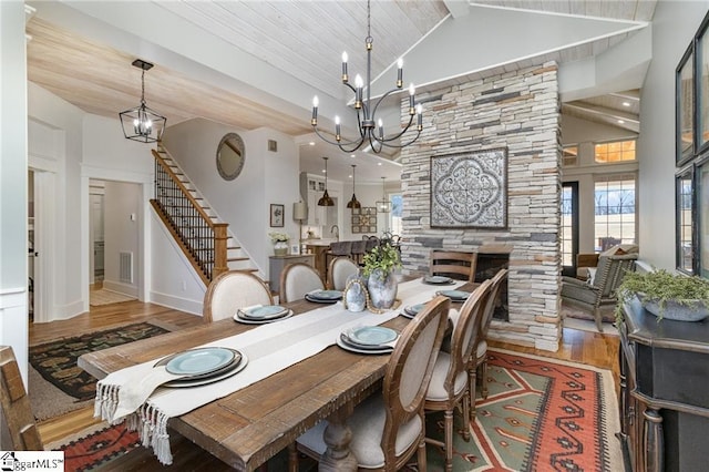 dining area with a fireplace, wood finished floors, visible vents, stairs, and an inviting chandelier