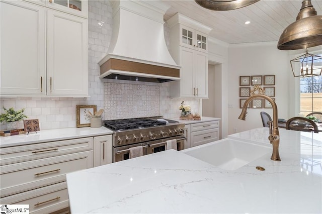 kitchen featuring decorative backsplash, custom range hood, hanging light fixtures, double oven range, and a sink