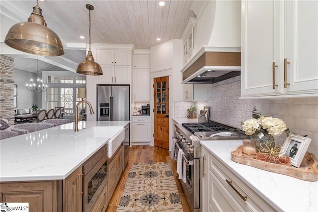 kitchen featuring tasteful backsplash, high end appliances, custom exhaust hood, white cabinetry, and a sink