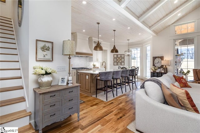 living area featuring lofted ceiling with beams, light wood-style floors, wood ceiling, and stairway