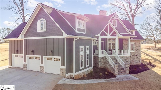 view of front of house featuring a chimney, an attached garage, board and batten siding, stone siding, and driveway