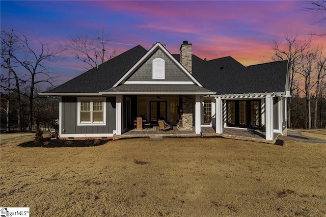 back of property at dusk with french doors, a chimney, a lawn, board and batten siding, and crawl space