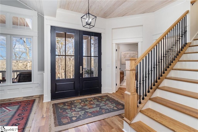 foyer featuring a decorative wall, wood finished floors, stairs, french doors, and an inviting chandelier