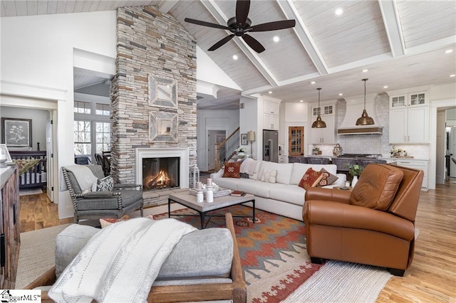 living area featuring light wood-style floors, a fireplace, high vaulted ceiling, and beamed ceiling