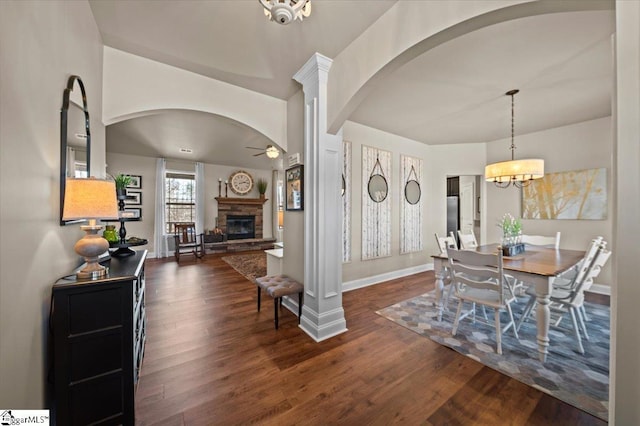 dining room with arched walkways, a fireplace, dark wood finished floors, and baseboards