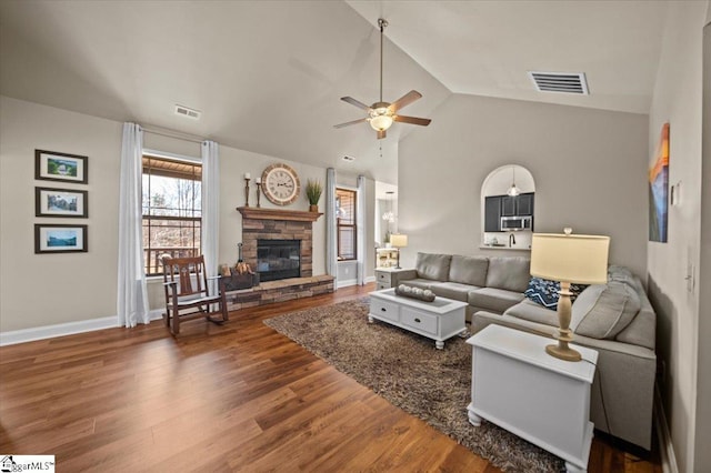 living area with a fireplace, wood finished floors, visible vents, baseboards, and vaulted ceiling