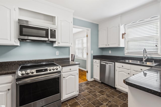 kitchen featuring stainless steel appliances, dark countertops, ornamental molding, white cabinetry, and a sink