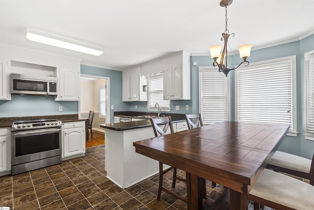 kitchen with appliances with stainless steel finishes, dark countertops, white cabinets, and ornamental molding