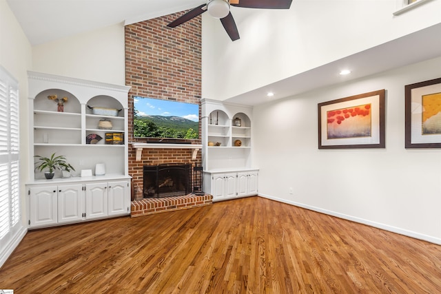 unfurnished living room featuring ceiling fan, high vaulted ceiling, wood finished floors, baseboards, and a brick fireplace