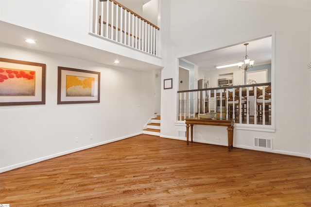 empty room featuring a chandelier, wood finished floors, visible vents, baseboards, and stairs