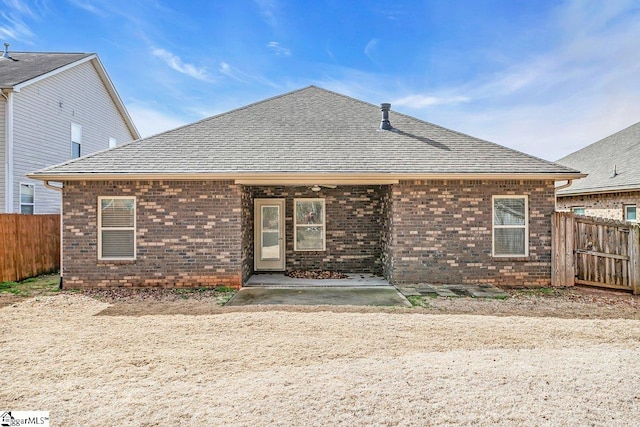 rear view of property with a shingled roof, fence, and brick siding