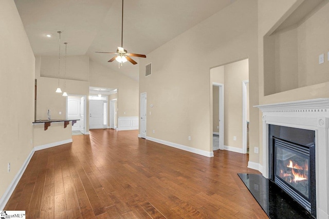 unfurnished living room with high vaulted ceiling, hardwood / wood-style flooring, visible vents, a ceiling fan, and a glass covered fireplace