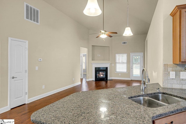 kitchen with light stone counters, visible vents, dark wood-type flooring, a glass covered fireplace, and a sink