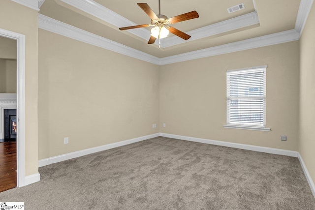 carpeted empty room featuring baseboards, visible vents, a raised ceiling, ceiling fan, and crown molding