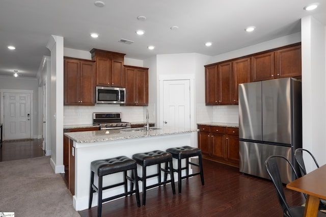 kitchen with a center island with sink, visible vents, decorative backsplash, appliances with stainless steel finishes, and a sink