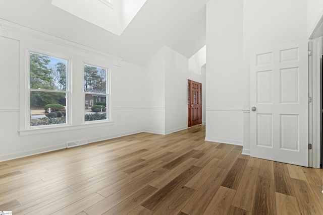 interior space featuring a skylight, visible vents, wood finished floors, high vaulted ceiling, and baseboards