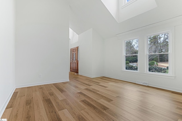 interior space with light wood-style floors, visible vents, a towering ceiling, and baseboards