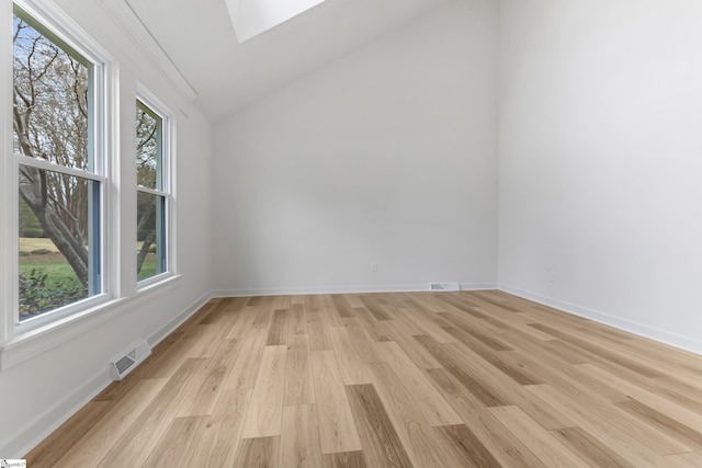 empty room featuring vaulted ceiling with skylight, baseboards, and light wood-style flooring