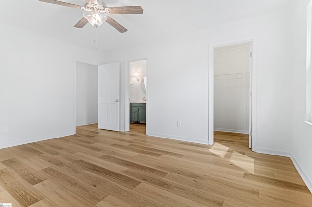 unfurnished bedroom featuring connected bathroom, baseboards, a closet, light wood finished floors, and a walk in closet