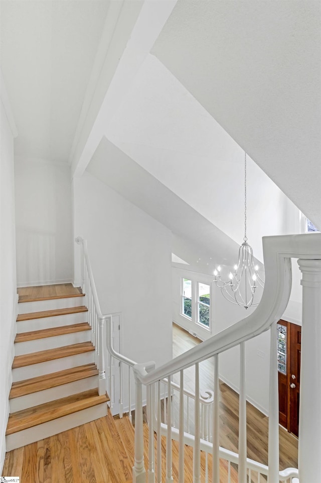 staircase with lofted ceiling, wood finished floors, and a notable chandelier