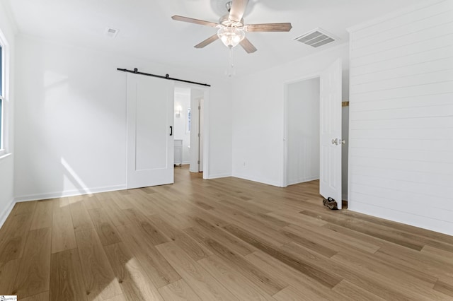 empty room featuring visible vents, ceiling fan, light wood-style flooring, and a barn door