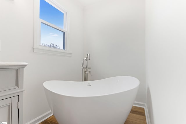 full bathroom with baseboards, a freestanding bath, and wood finished floors