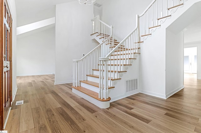 stairway with a high ceiling, wood finished floors, and visible vents