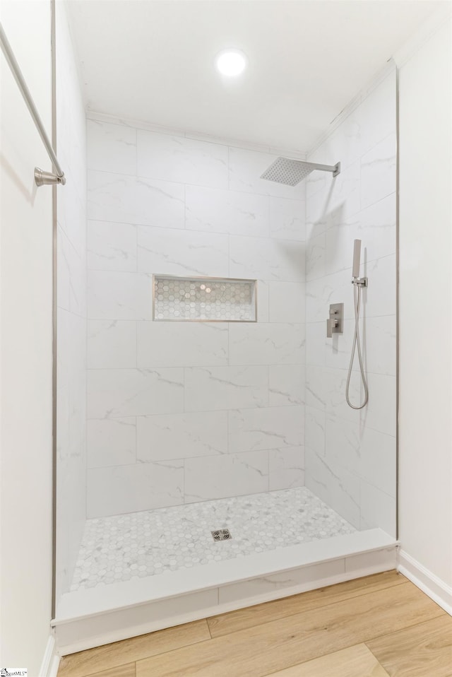 bathroom featuring wood finished floors, a tile shower, and baseboards