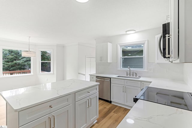 kitchen featuring appliances with stainless steel finishes, a sink, light wood-style flooring, and light stone counters