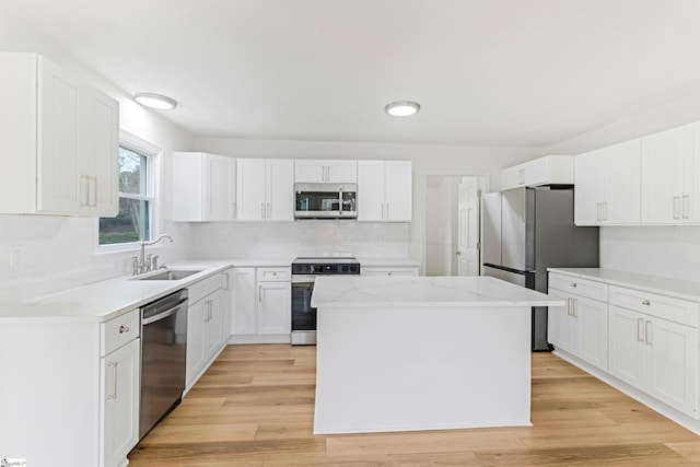 kitchen with white cabinets, light wood-style flooring, a kitchen island, appliances with stainless steel finishes, and a sink