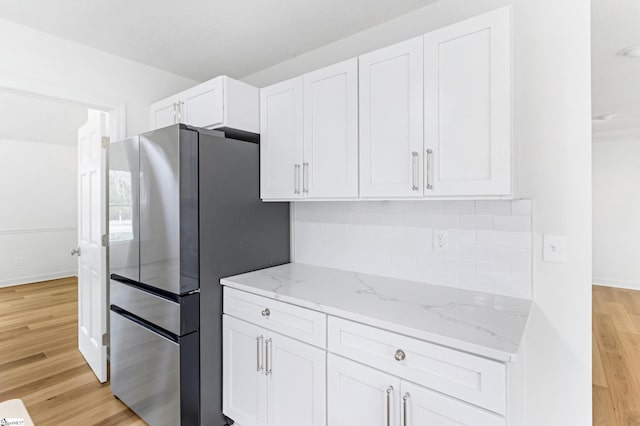 kitchen with tasteful backsplash, light wood-type flooring, freestanding refrigerator, and white cabinetry