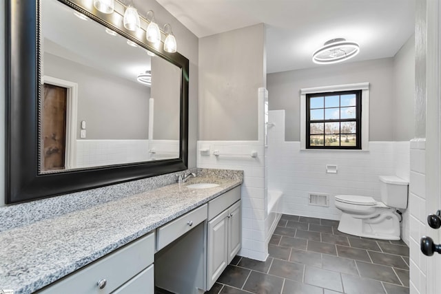 bathroom featuring visible vents, toilet, a wainscoted wall, vanity, and tile walls