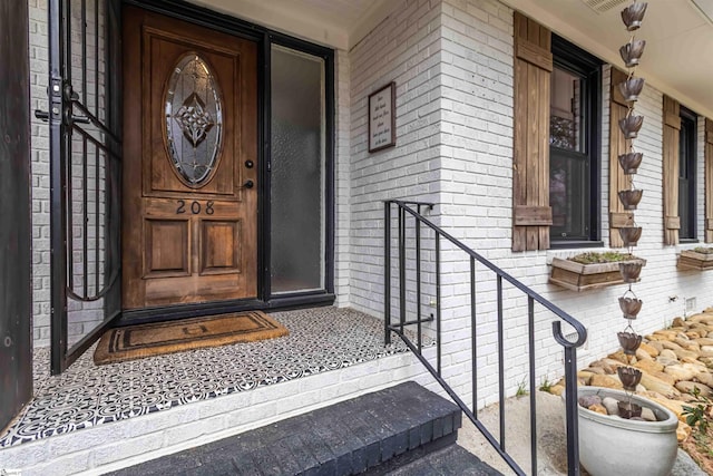 doorway to property with brick siding, a porch, and visible vents