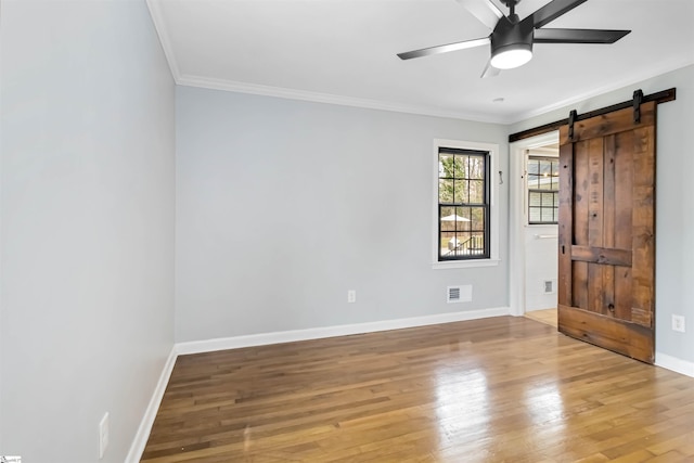 unfurnished room with crown molding, light wood-style flooring, a barn door, a ceiling fan, and baseboards