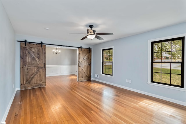 spare room with visible vents, light wood-style flooring, a barn door, ceiling fan, and baseboards