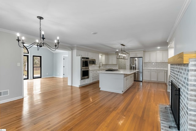 kitchen with tasteful backsplash, stainless steel appliances, crown molding, light countertops, and a notable chandelier